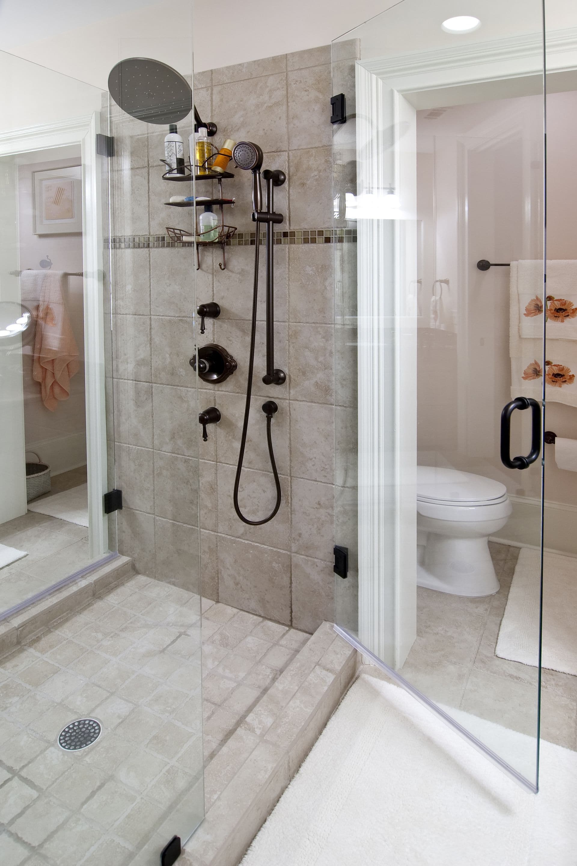 Spacious bathroom featuring a glass-enclosed shower with beige tiles, a sleek black shower system, and adjacent white toilet, conveying a clean, modern feel.