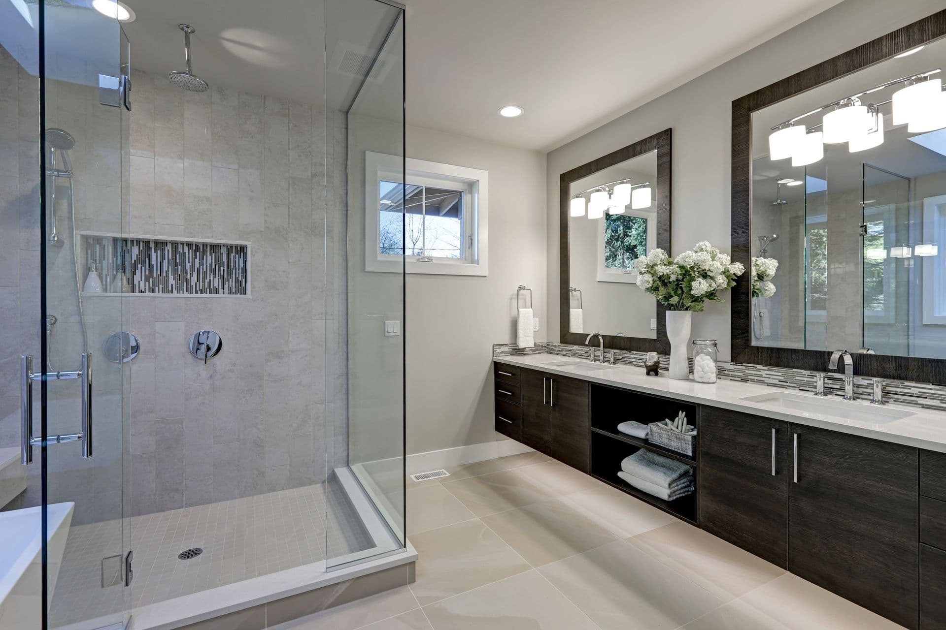 Modern bathroom with a glass-enclosed shower, double sinks on a dark wood vanity, large mirrors, and elegant lighting. Bright, sleek, and luxurious.