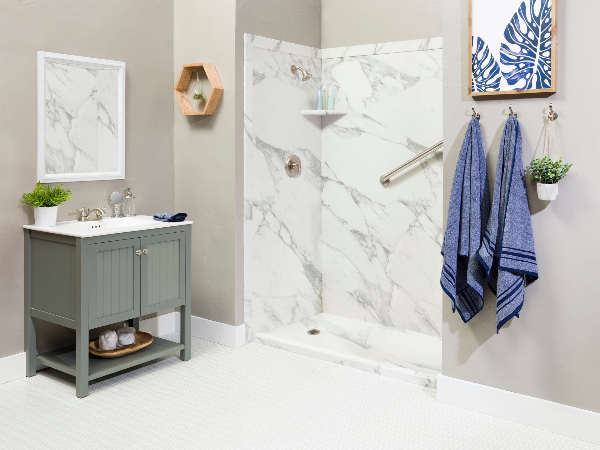 Modern bathroom with a marble shower, silver fixtures, and blue towels. A small vanity with plants and framed art add a fresh, calming touch.