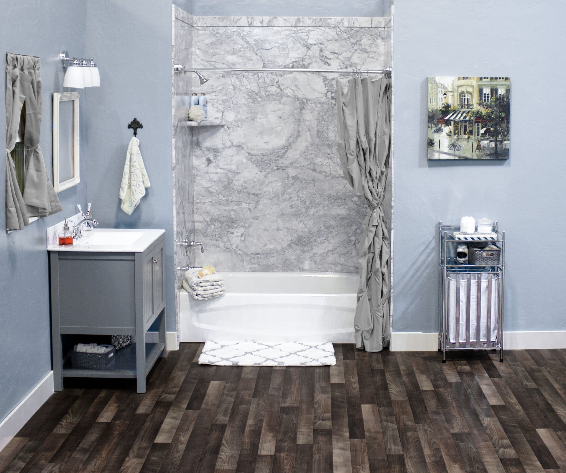 Stylish bathroom with gray marble shower, dark wood floor, gray vanity, and art on blue walls. Features a metal shelf and plush towels for a cozy feel.